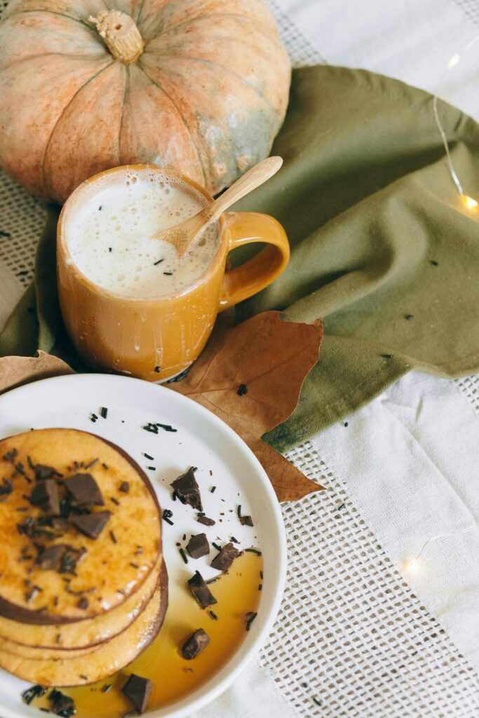 Warm autumn breakfast scene featuring pancakes with syrup and a pumpkin spice latte.